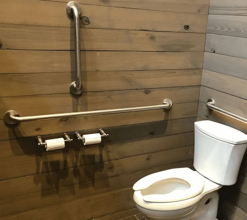 Brushed stainless grab bar mounted on a wood-look wall beside a toilet in a DFW home